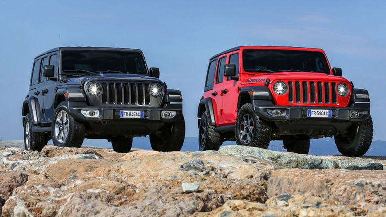 A dark grey and a red colored Jeep Wrangler on top of a rocky surface.
