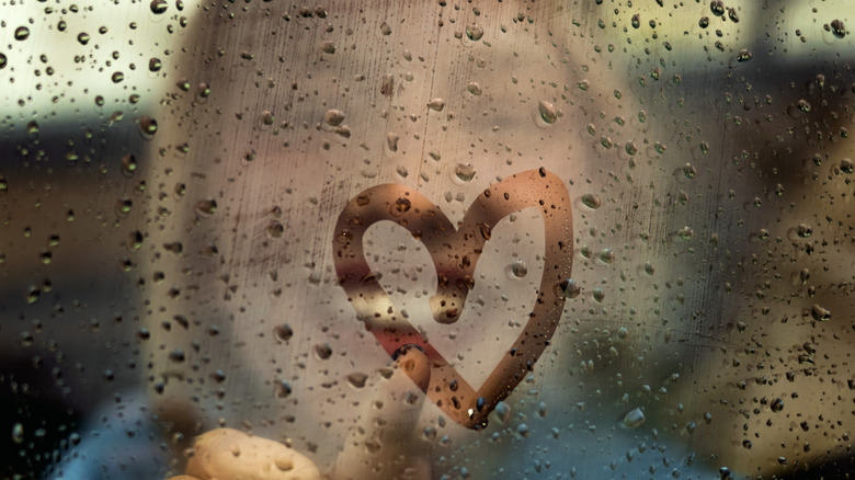 person drawing a heart on a foggy car window