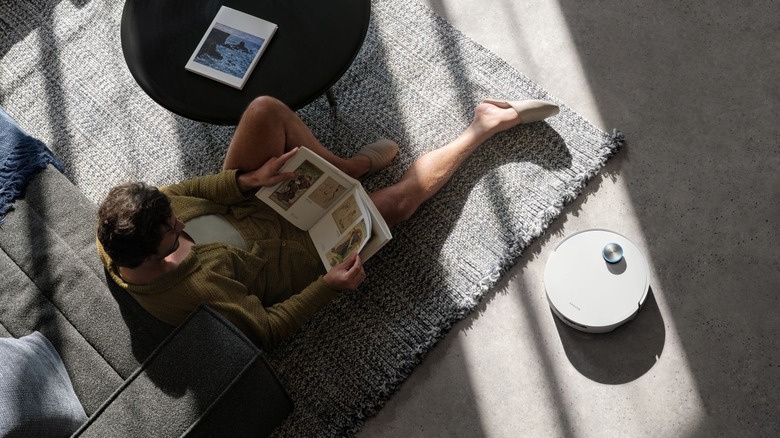 The Dreame Aqua10 Ultra Roller cleaning near a man on a rug.