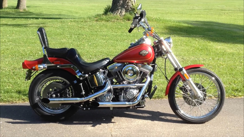 A cherry red Harley Davidson FXST Softail parked next to a lawn on a sunny day