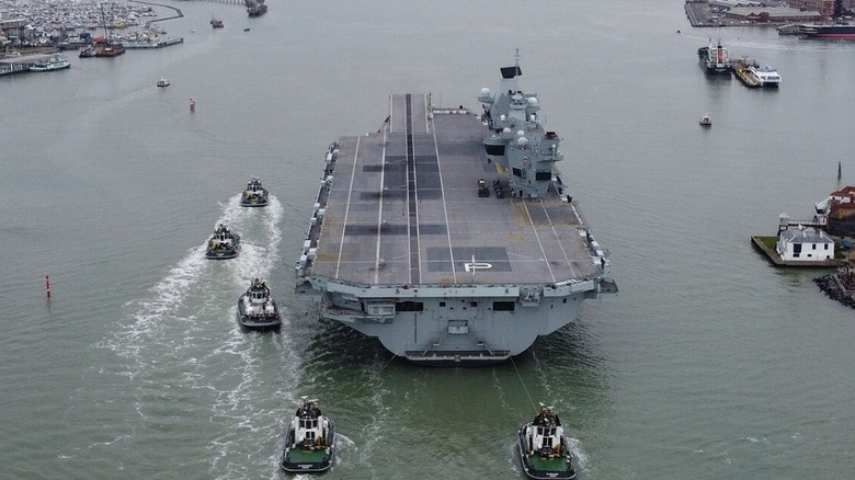 UK aircraft carrier HMS Prince Of Wales being guided by tugs entering port