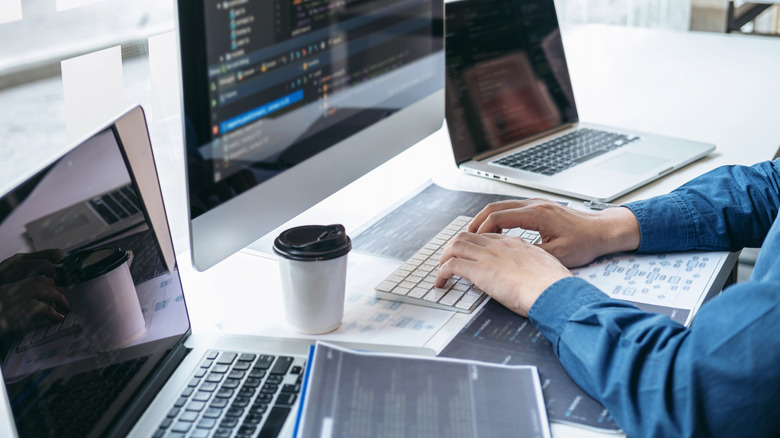 Man working on desktop with laptops open beside him