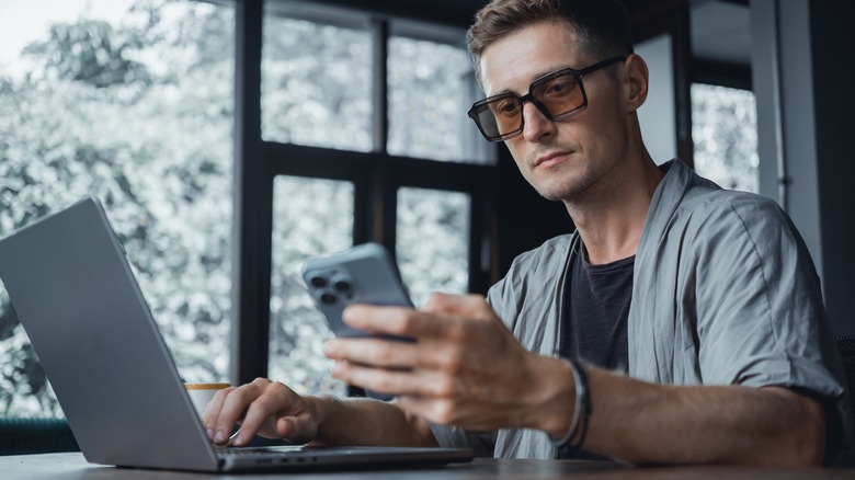 man using iphone and laptop