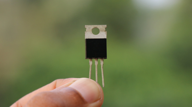 A person holding a power transistor between their fingers