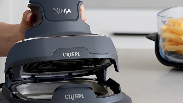 Ninja Crispi air fryer base open on a counter next to a glass container filled with french fries.