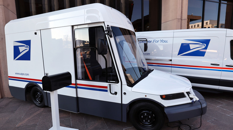 Side view of a USPS NGDV. A United States Postal Service battery-powered vehicle on show at an event announcing its launch at the Postal Service Headquarters on December 20th 2022, in Washington, DC. The vehicle is shown next to a mailbox and plugged into an electric charger.