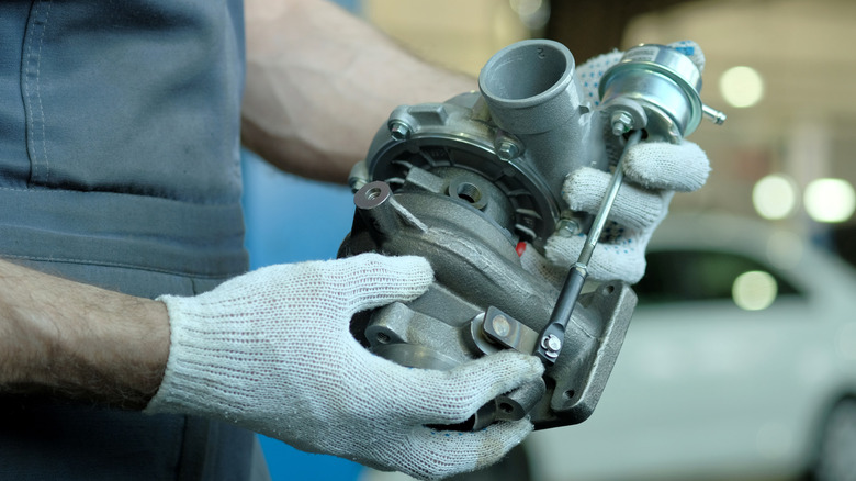 A gloved mechanic holding and preparing to install a new turbocharger