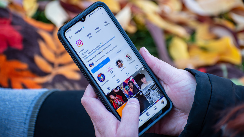 Hands holding a smartphone with Instagram profile on the screen.