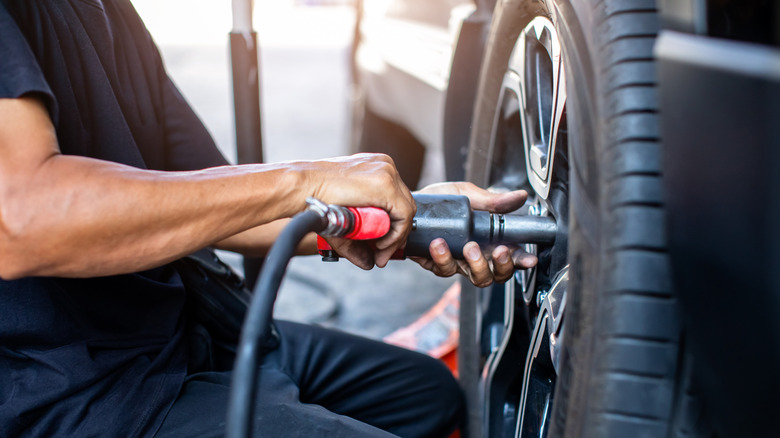 A mechanic holding an impact wrench to a car wheel.