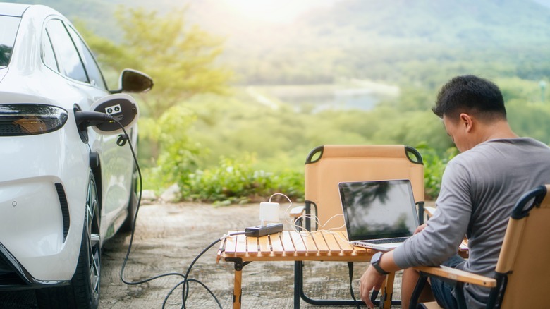 Businessman online working and relaxing outdoor activity using V2L technology where an electric vehicle acts as a mobile battery.
