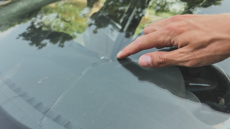 Someone pointing at a crack on the windshield in front of the driver side