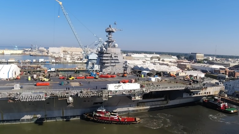 Support ships maneuver USS John F. Kennedy in river