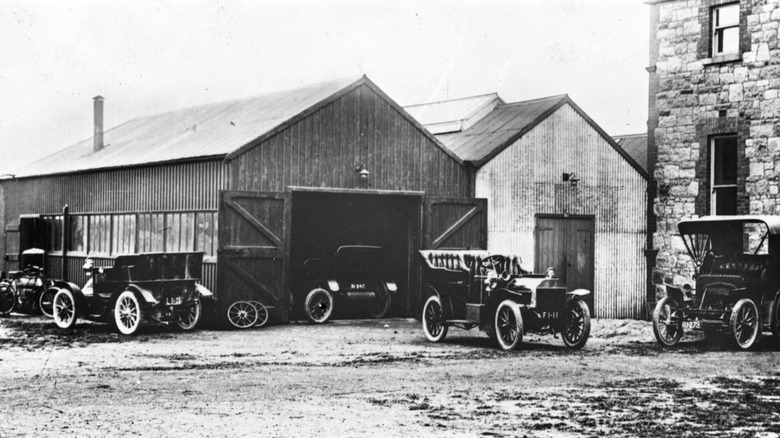 Early automobiles from around the turn of the 19th century parked in front of a garage.