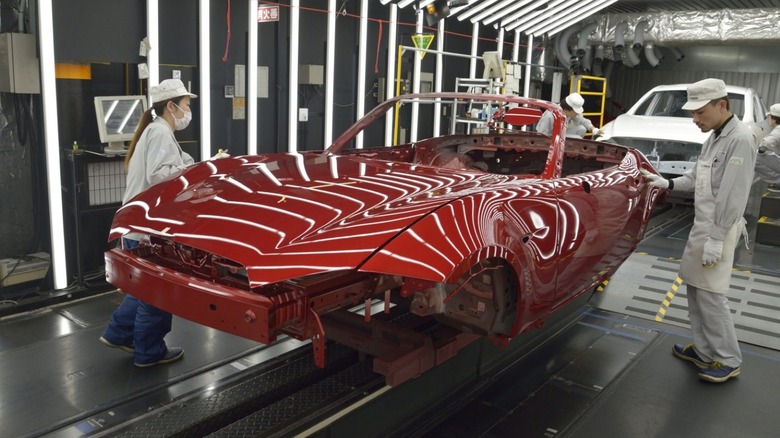 Artisans in a Mazda car shop finishing a car body with Soul Red Crystal Takuminuri paint.