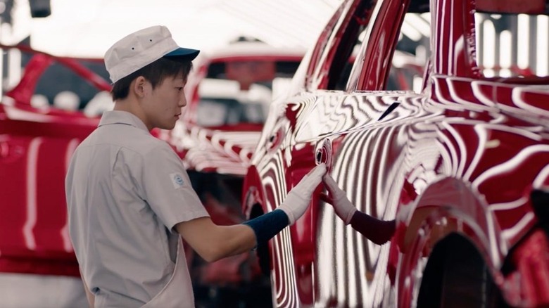 An artisan on a production line finishing a Mazda car in Soul Red Crystal