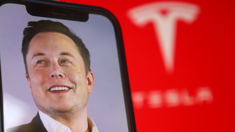 A picture of Elon Musk on a smartphone with the Tesla logo in the background