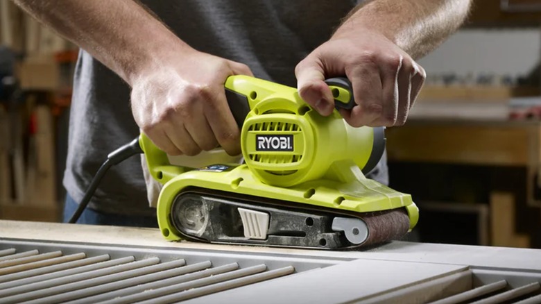 A person using a Ryobi belt sander on a door.