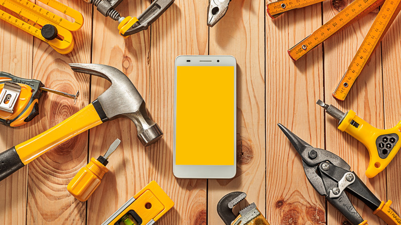 Cell phone with yellow screen on wood table surrounded by tools