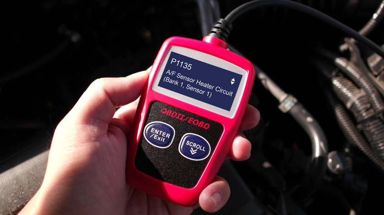 A person holding a red OBD scan tool that's currently showing a P1135 error code.