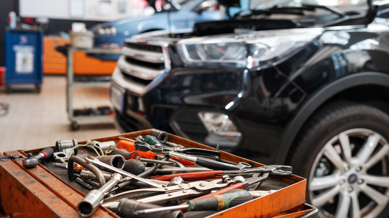 A black SUV parked in a repair shop with tools in front on an orange toolbox.