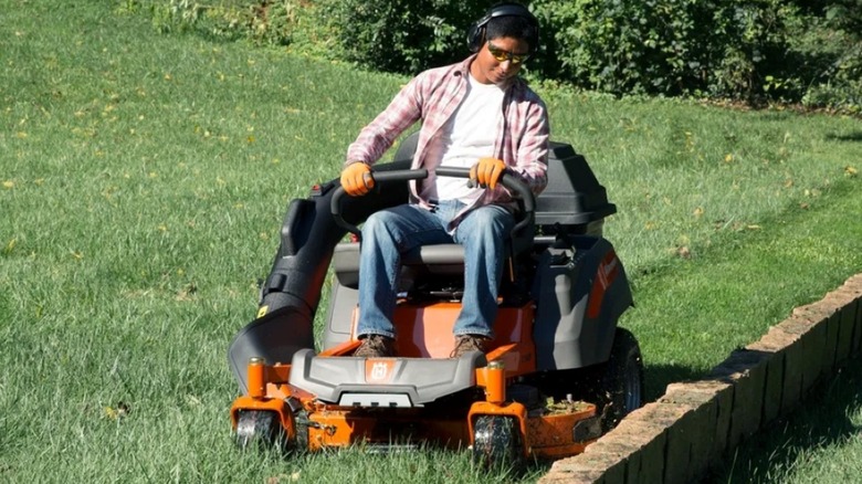 Using a Husqvarna zero-turn mower to mow along a stone retaining wall.