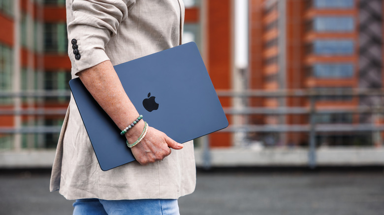 Woman walking and holding a closed Macbook under her arm