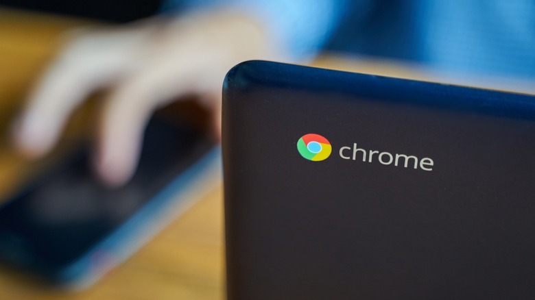 a Chromebook with a user in the background reaching for a phone