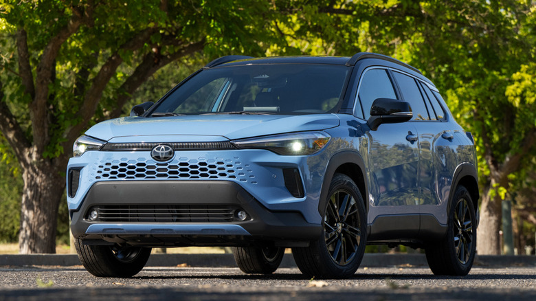 Blue Toyota Corolla Cross Hybrid parked on a leafy rural road