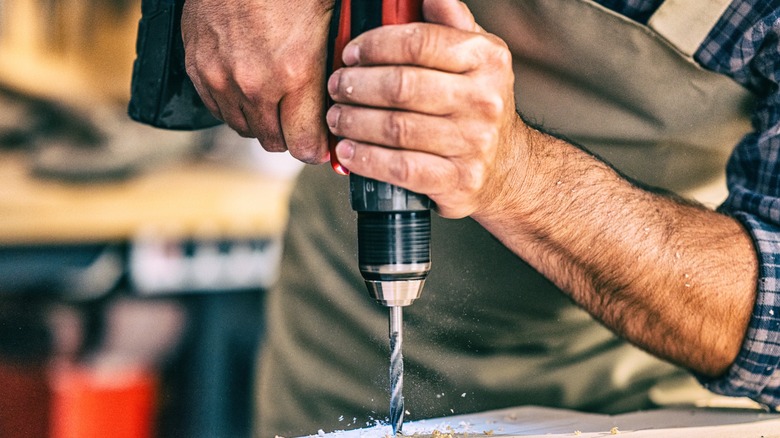 Holding a hand power drill securely with two hands.