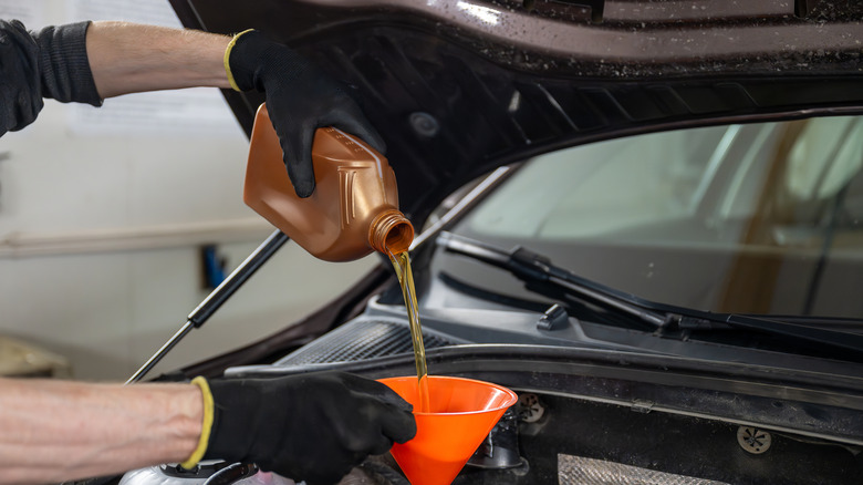 A gloved mechanic pouring oil into a car engine through a funnel