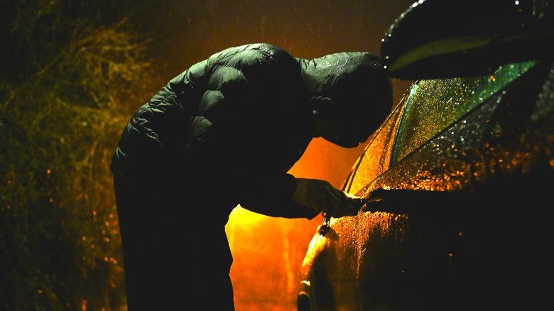 A person in a hoodie breaking into a car at night
