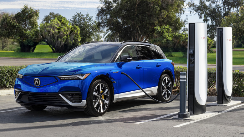 A blue Acura ZDX charging with a Tesla Supercharger