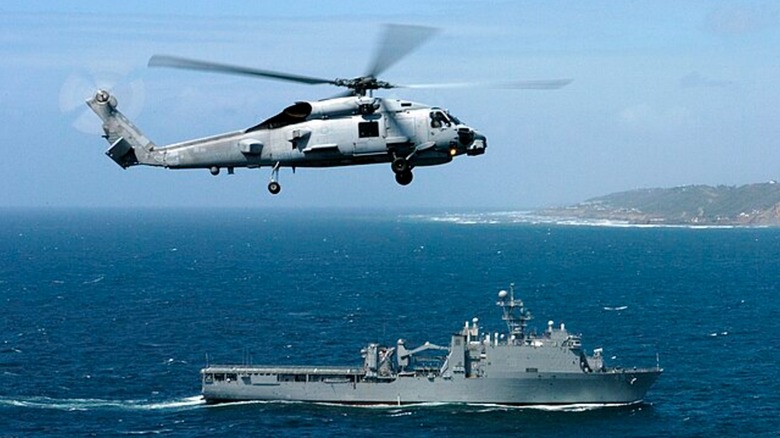 An MH-60R Seahawk in the sky above a destroyer
