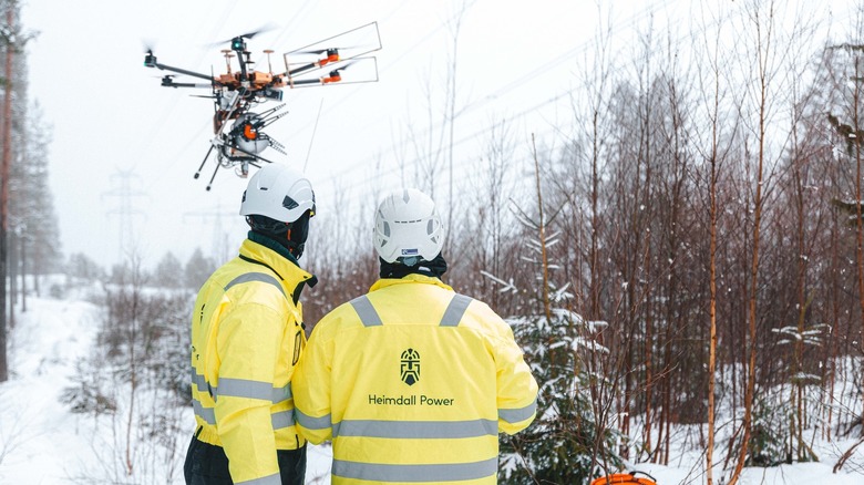Workers watch as a drone flies off to install a Neuron
