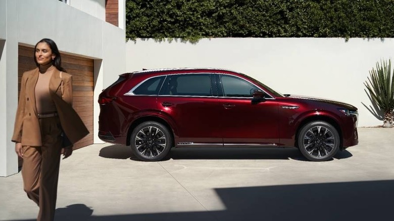 2025 Mazda CX-90 luxury SUV in red parked in a modern driveway with stylish woman walking nearby