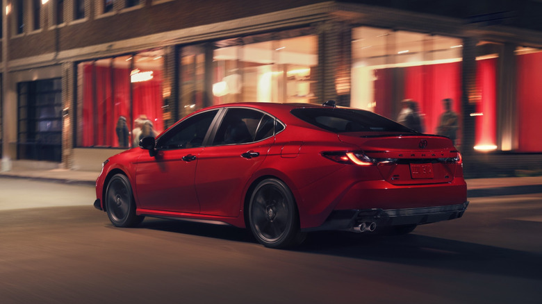 A night time rear-end view of a red 2026 Toyota Camry being driven through town.