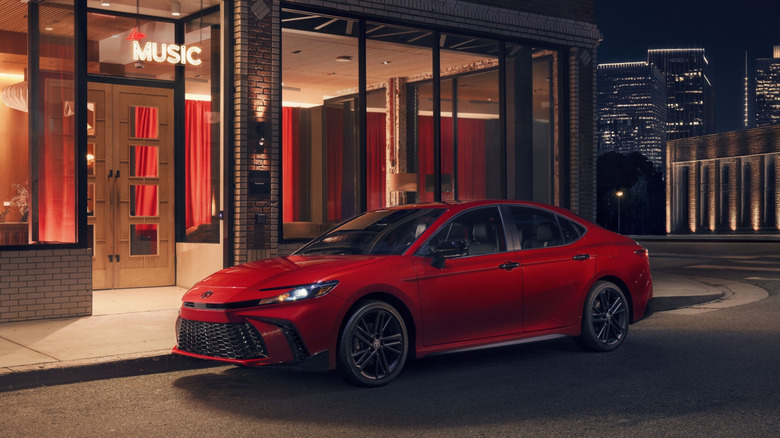 A red 2026 Toyota Camry parked in an urban night setting in front of a music bar.