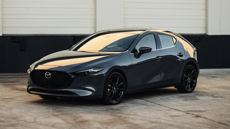 A gray Mazda 3 parked in front of an industrial building.