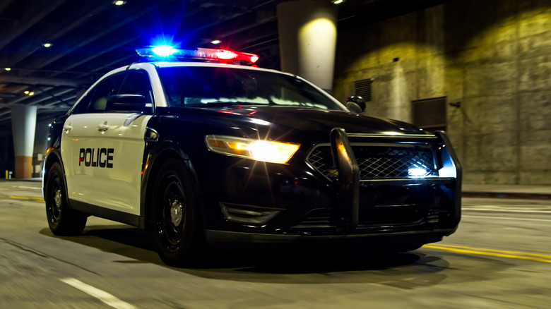 A police car driving through an underpass at night with its siren lights turned on.