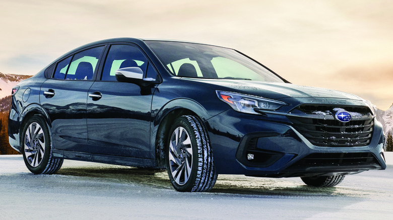 A black Subaru Legacy sedan against a snowy, mountainous background.