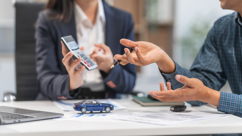 Two people discussing documents, with a model car and car keys on the table