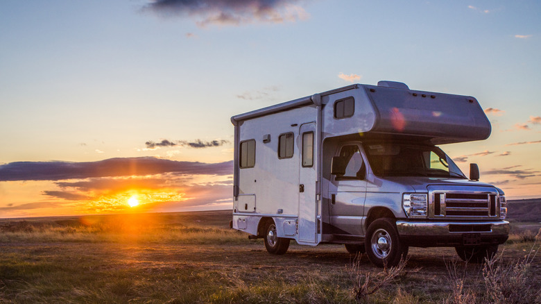 A debadged Ford Econoline-based RV in a field, front 3/4 view, sunset in the background