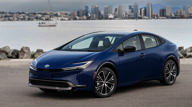 2026 Toyota Prius parked by waterfront with city in background, front-left 3/4 view