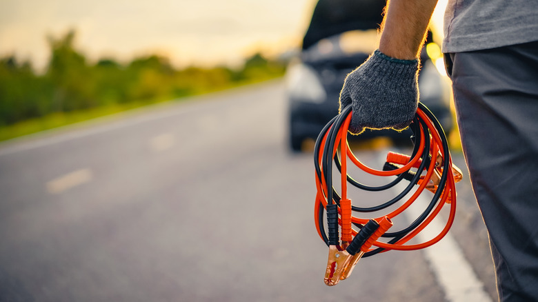 Man walking to car holding jumper cables