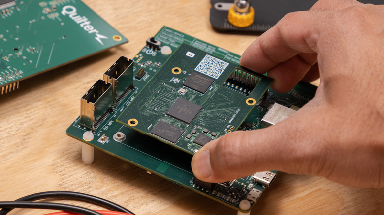 A hand placing a PCB board on top of the mainboard on a wooden desk