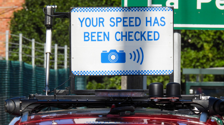 Road sign saying "Your speed has been checked" mounted on the roof of a red car.