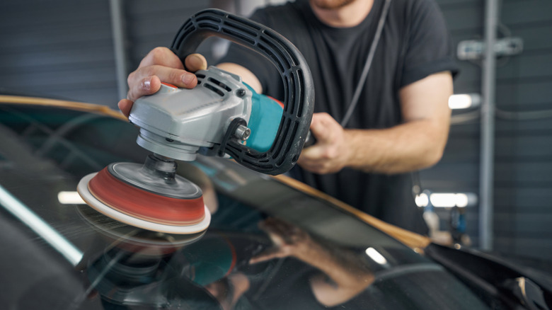 A person detailing a car windshield with a buffer