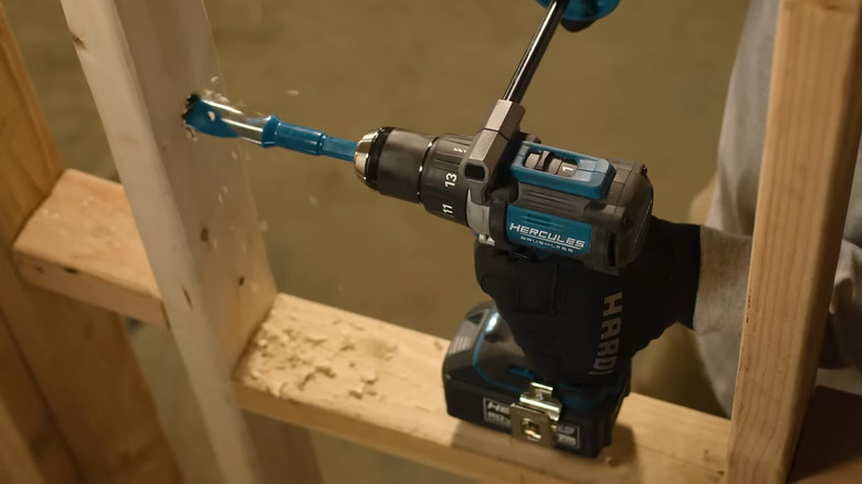 A person using the Hercules HCB91K1 cordless drill to drill holes in wood beam