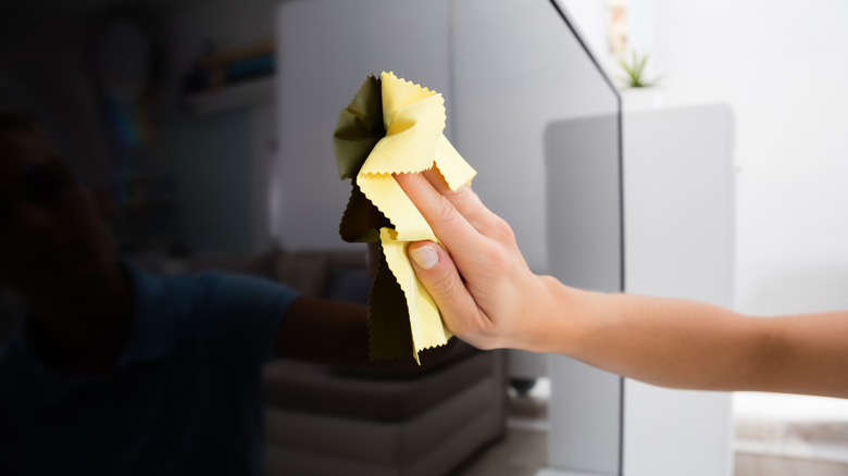 Close-up Of Woman Using Cloth To Clean The Television At Home