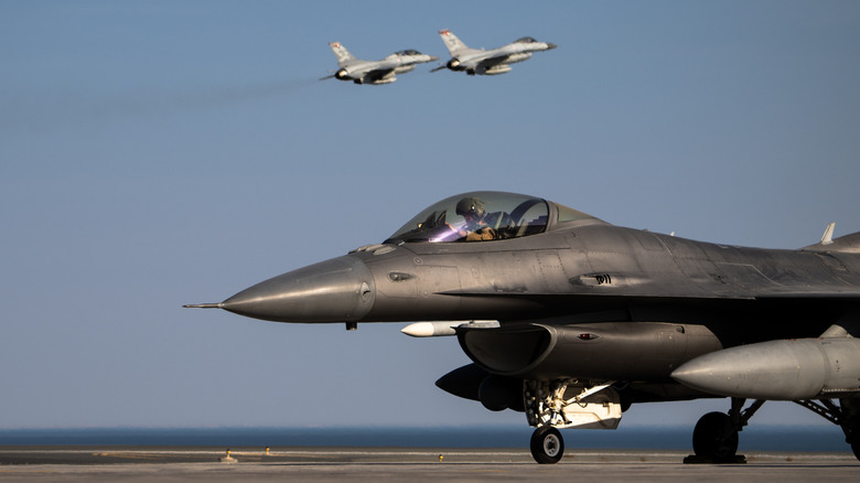 US Air Force F-16 prepares to take off at commander center as two F-16s fly in the sky
